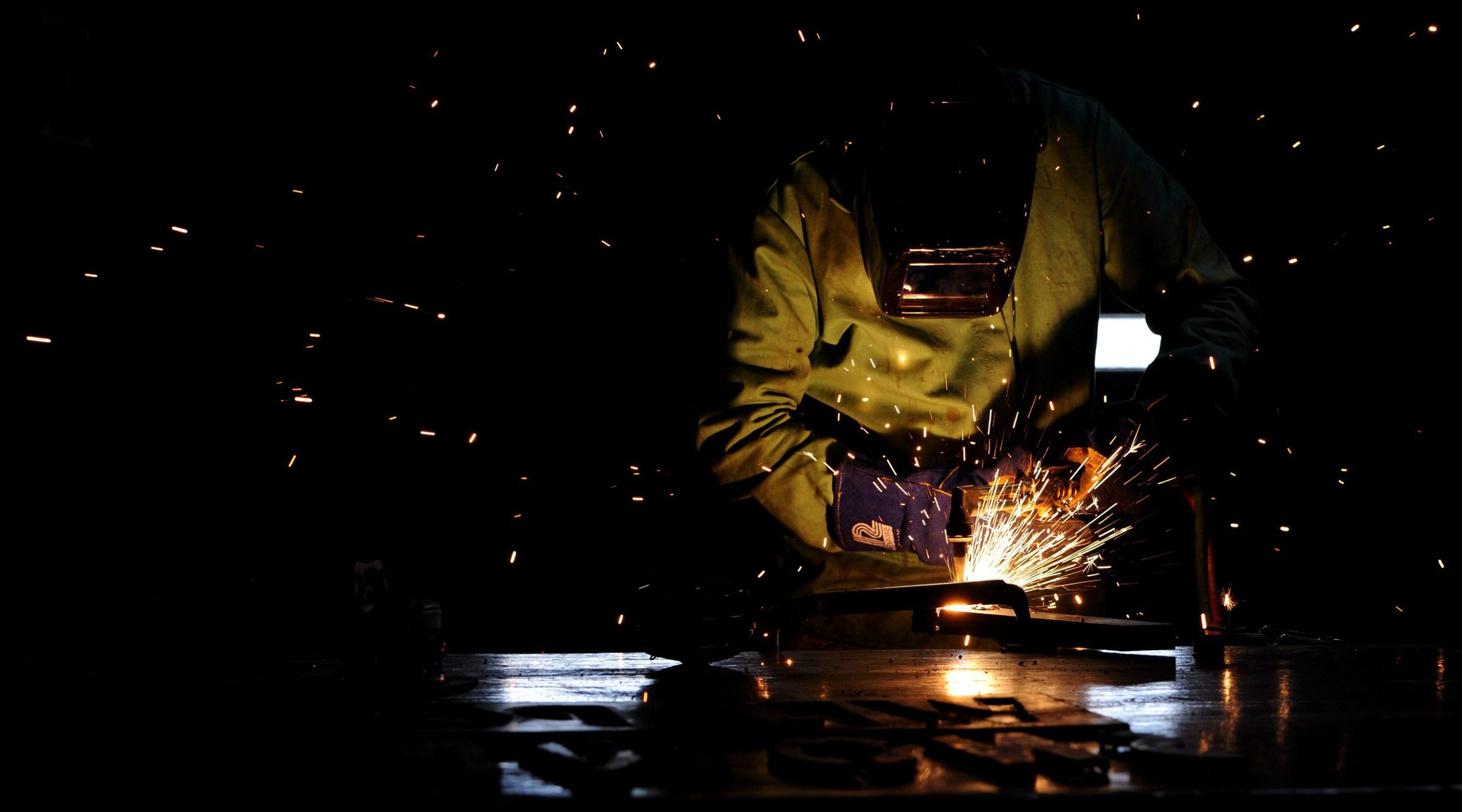 A welder working in a dark workshop with sparks flying