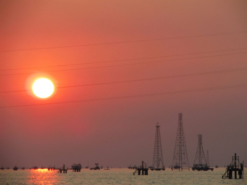 Oil derricks on the water at sunset