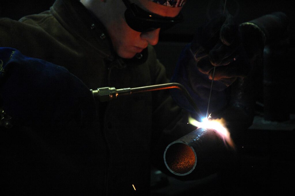 A welder cutting a steel pipe with a gas torch